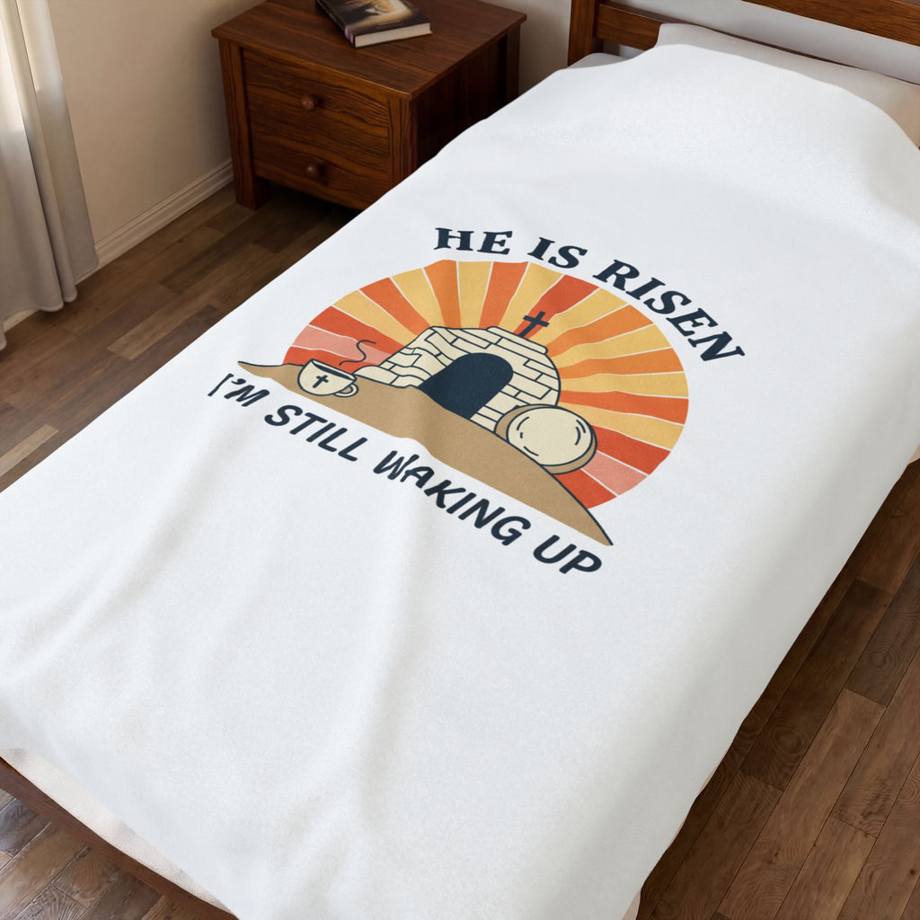Blanket with 'He is Risen, I'm Still Waking Up' design on a bed in a bedroom.