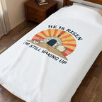 Blanket with 'He is Risen, I'm Still Waking Up' design on a bed in a bedroom.