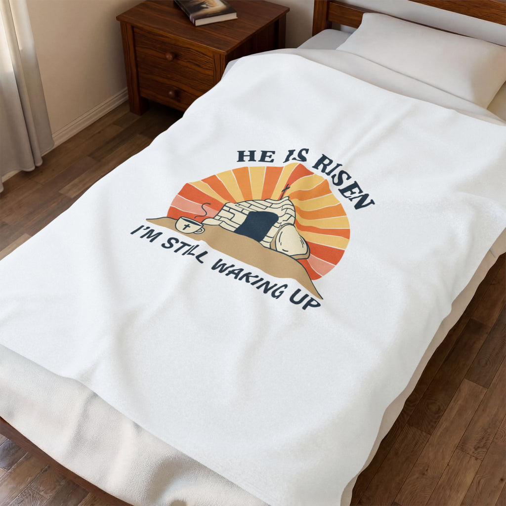 Blanket with 'He is Risen, I'm Still Waking Up' design draped over a bed.